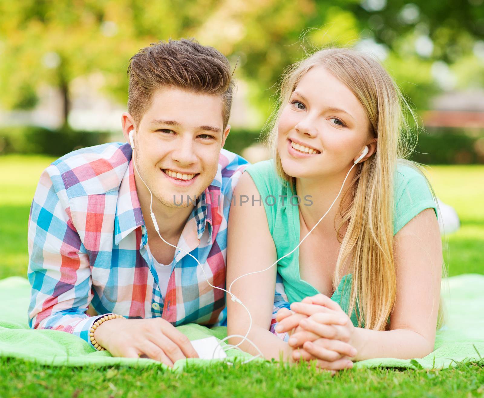 vacation, holidays, technology and friendship concept - smiling couple with smartphone and earphones lying on blanket in park