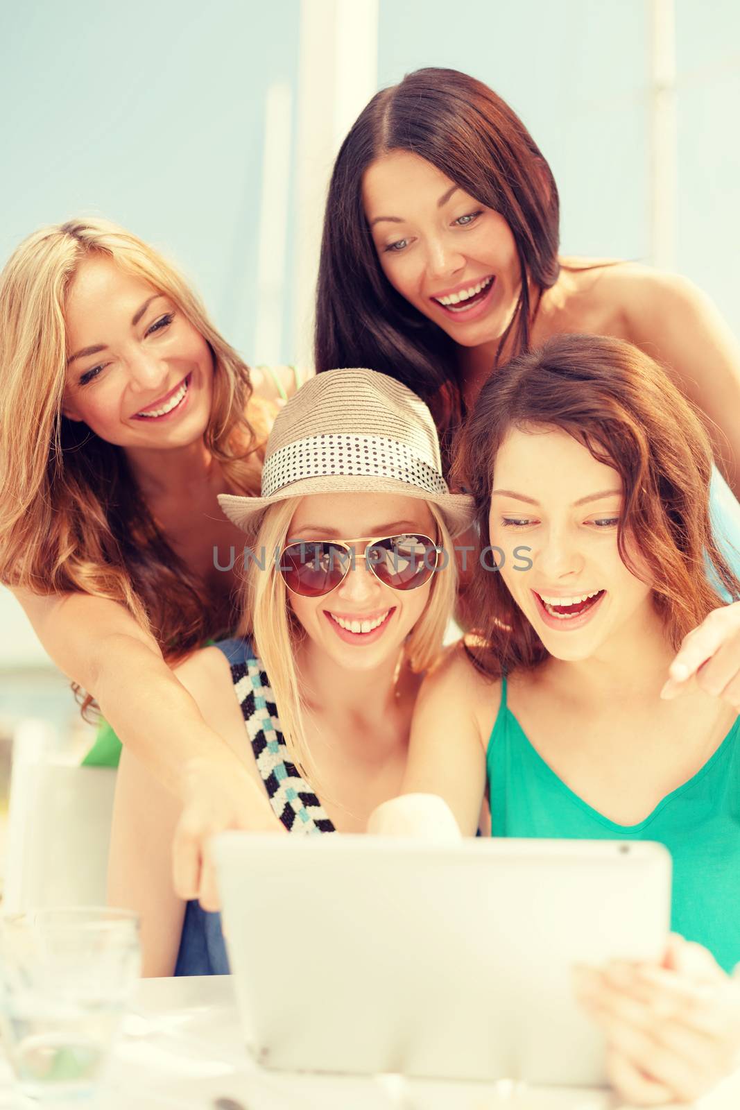 smiling girls looking at tablet pc in cafe by dolgachov