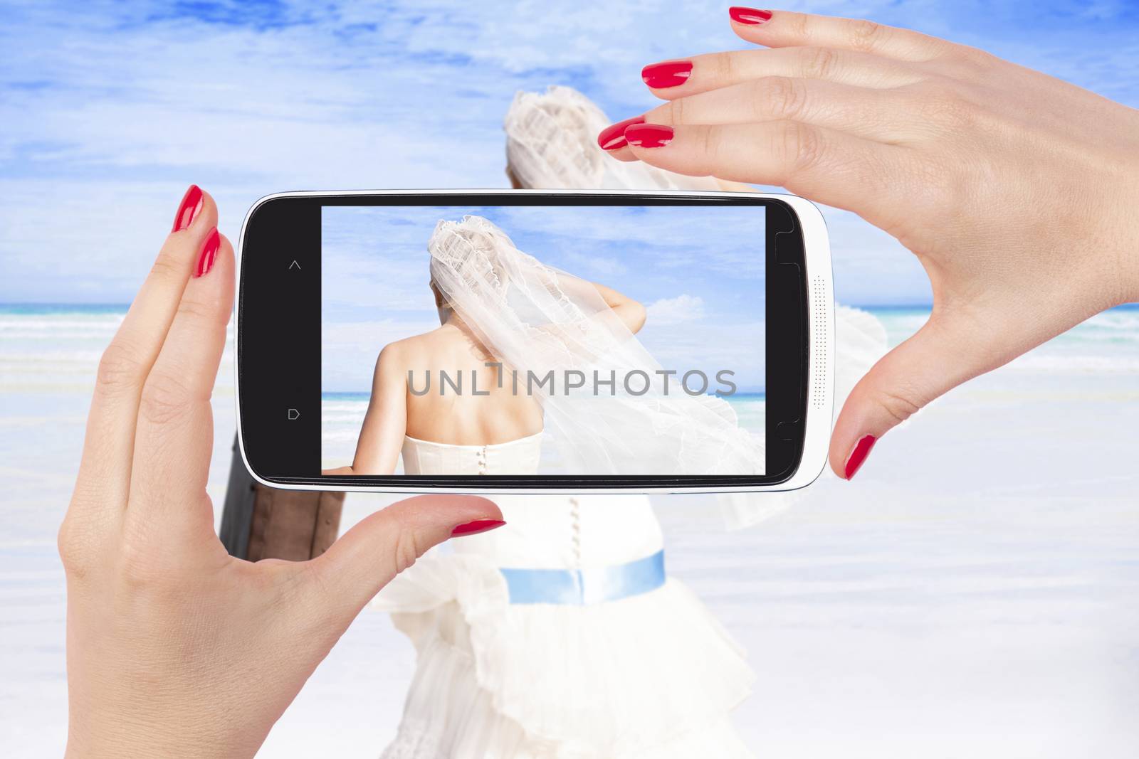 Taking picture of beautiful bride on tropical island with white sand with smartphone. Selfie and beach wedding. 