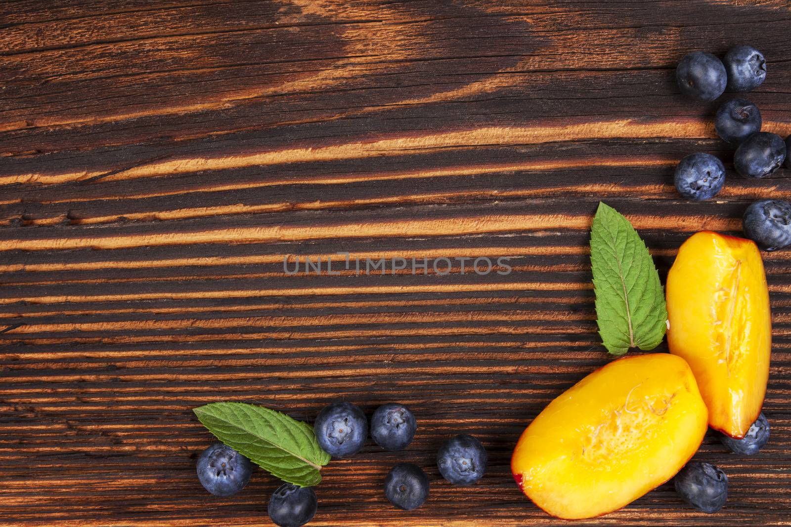 Fresh fruit background with copyspace. Blueberries and nectarines and mint leaves on wooden background, top view.