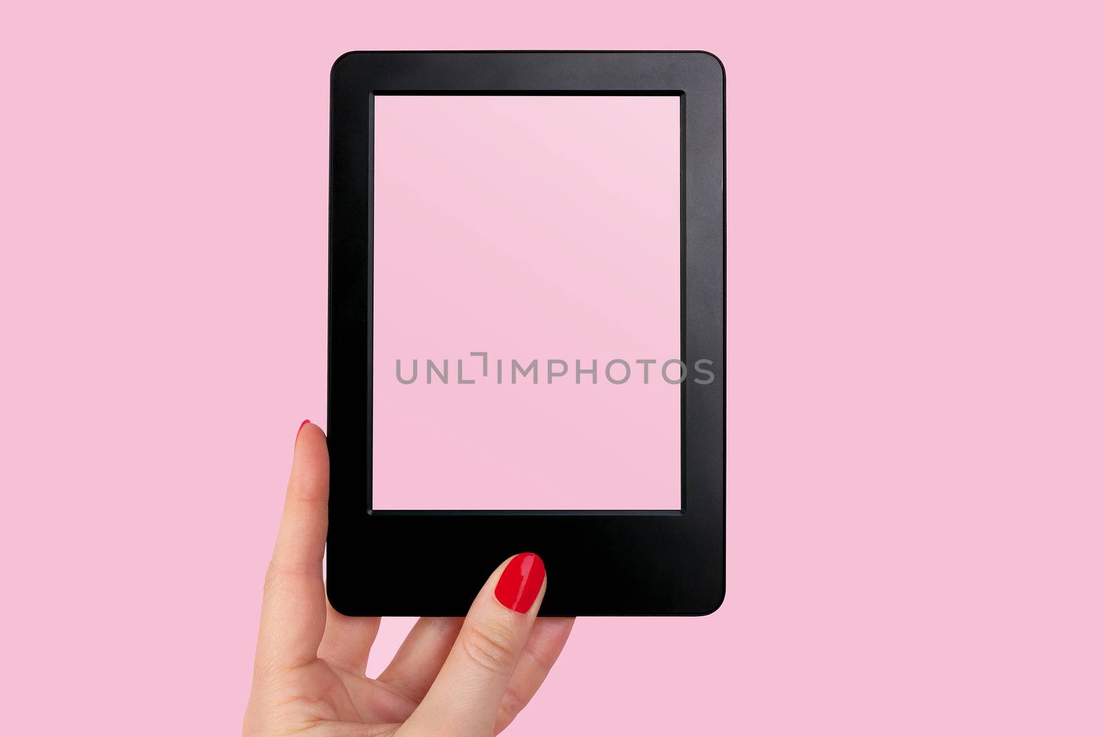 Female hand with red nails holding e reader against pink background. Modern book reading. 