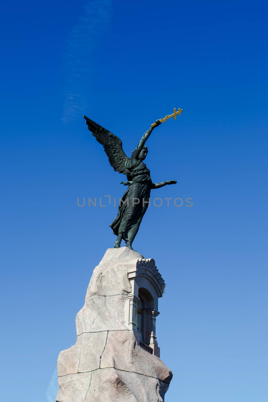 Angel woman sculpture on a rock with a cross holding on hand, on navy blue sky background.