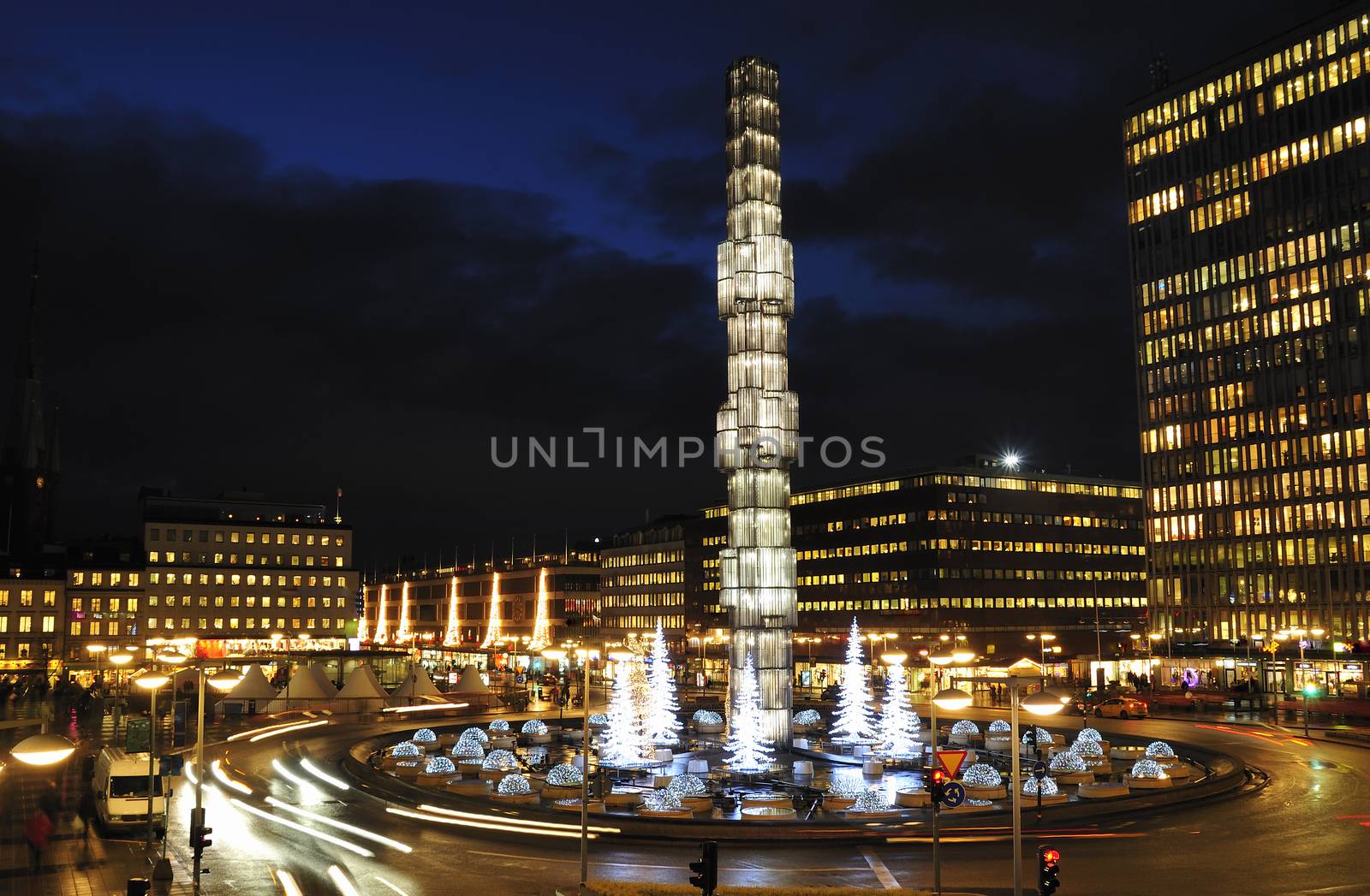 The iconic Kristall obelisk illuminated in the centre of Sergels torg, the modern public square in the heart of Stockholm, overlooking the pedestrianised plaza, traffic roundabout, Kulturhuset, shops and office buildings glowing under the blue dusk sky.