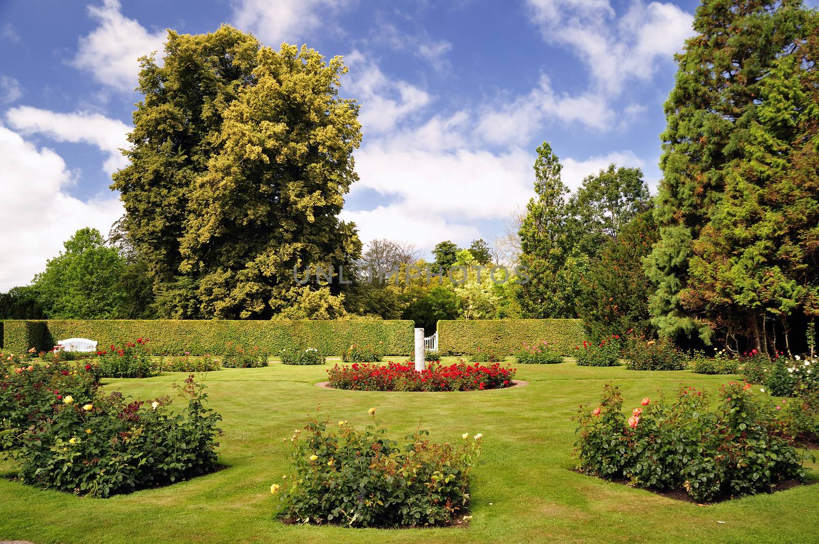 Neatly trimmed lawn, sculpted foliage and colorful flower beds under a clear blue sky.