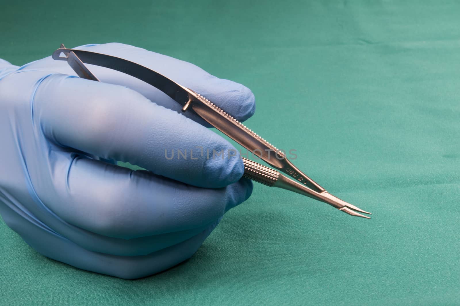 Surgeon holding micro surgical tool.Surgeon hand in blue glove.Surgeon holding Micro-needle holder,curved,short model.The background is blue tablecloth operating