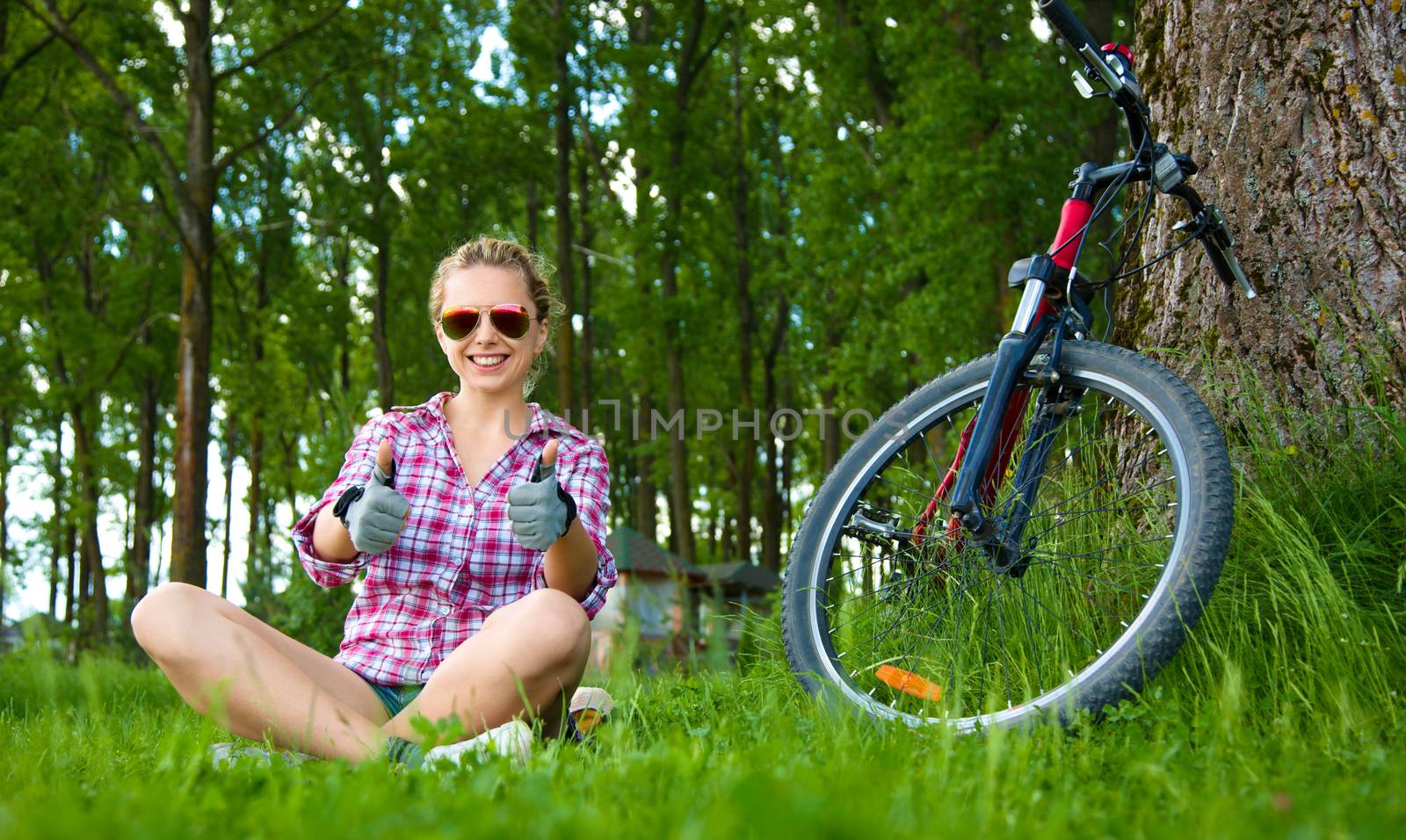 Young cyclist sitting in the fresh green grass and showing thumbs up gesture