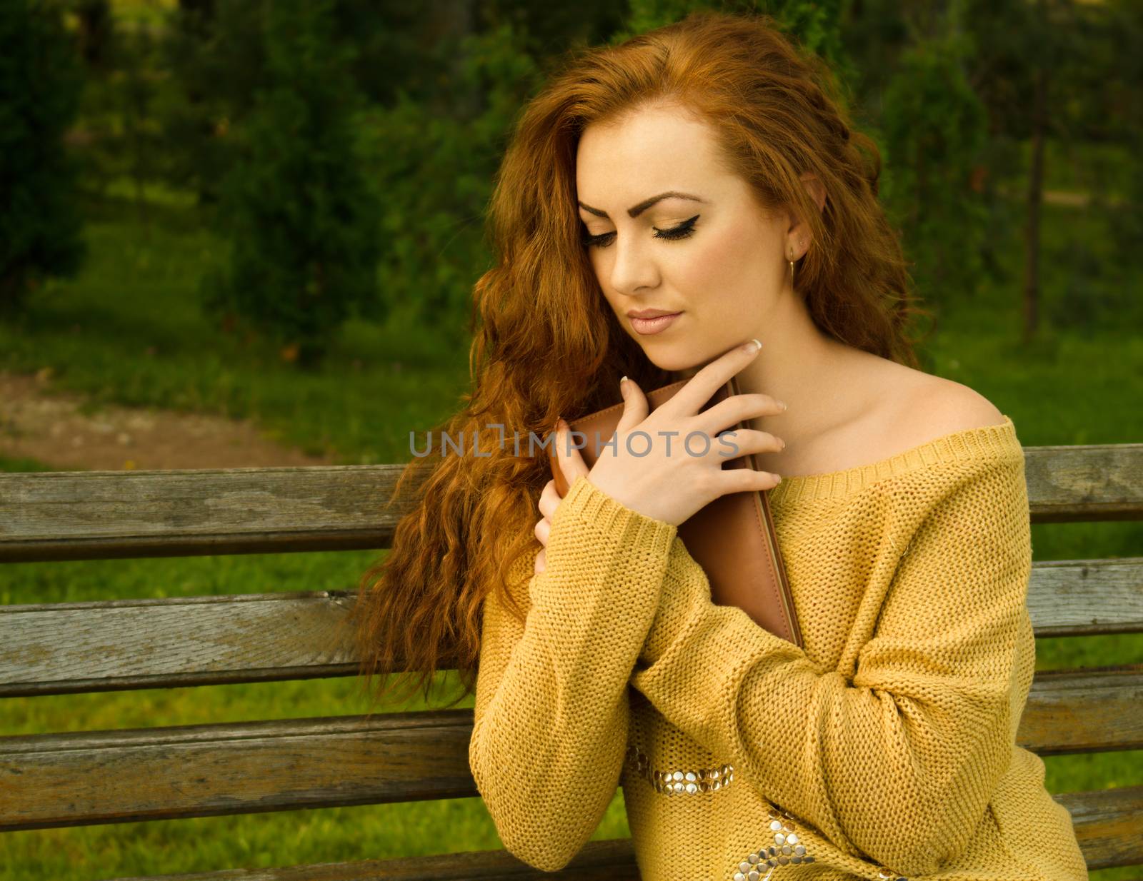Ginger-haired woman sitting on a bench with book in the park