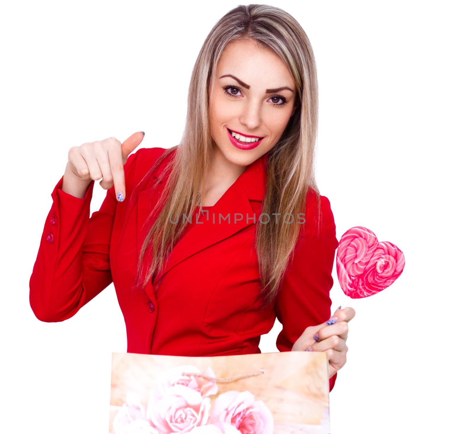 Smiling young woman with heart shaped lollipop and present bag isolated on white