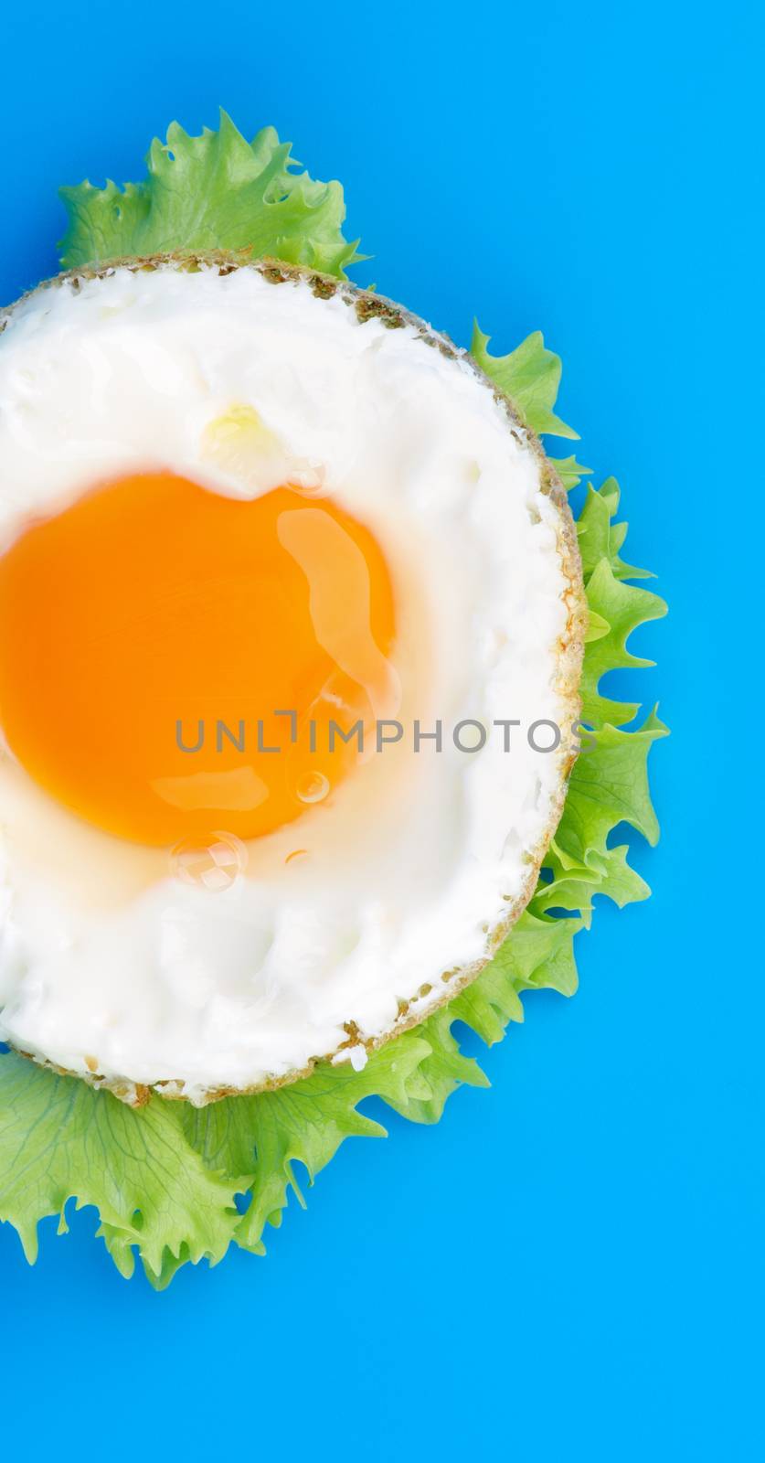 Half of Fried Eggs Sunny Side Up with Lettuce on Blue background. Top View