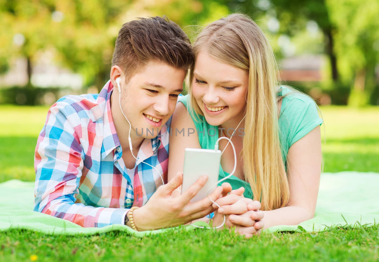 vacation, holidays, technology and friendship concept - smiling couple with smartphone and earphones making selfie in park