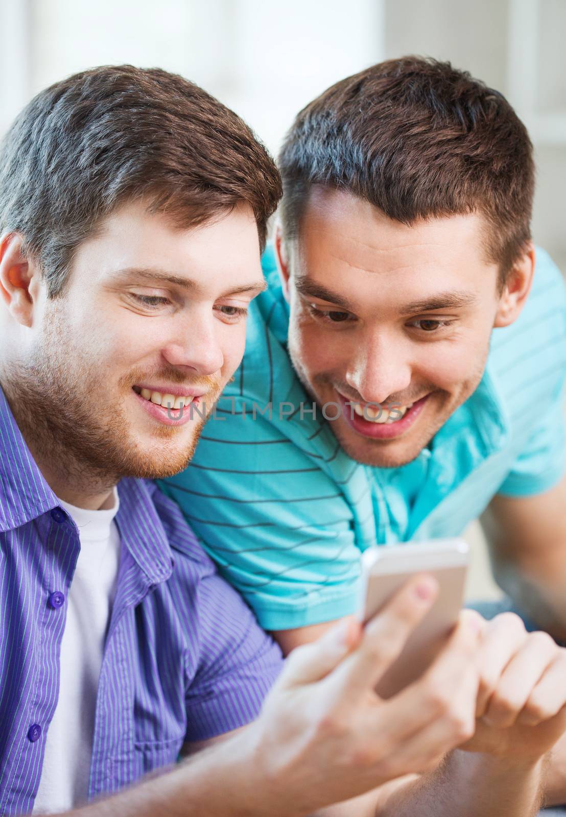 friendship, technology, drinks and home concept - smiling male friends with smartphone at home