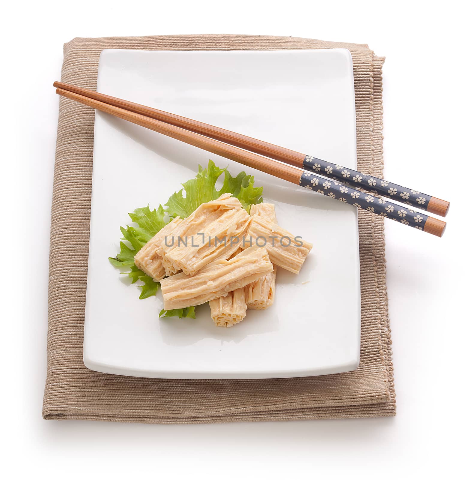 Some pieces of tofu skin with fresh green lettuce and chopstick on the white plate