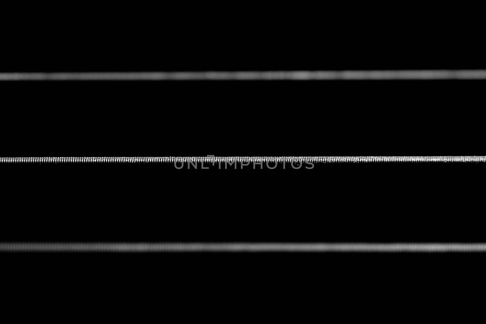 A dramatic 1:1 macro shot of acoustic guitar strings framed horizontally across the frame in black and white.