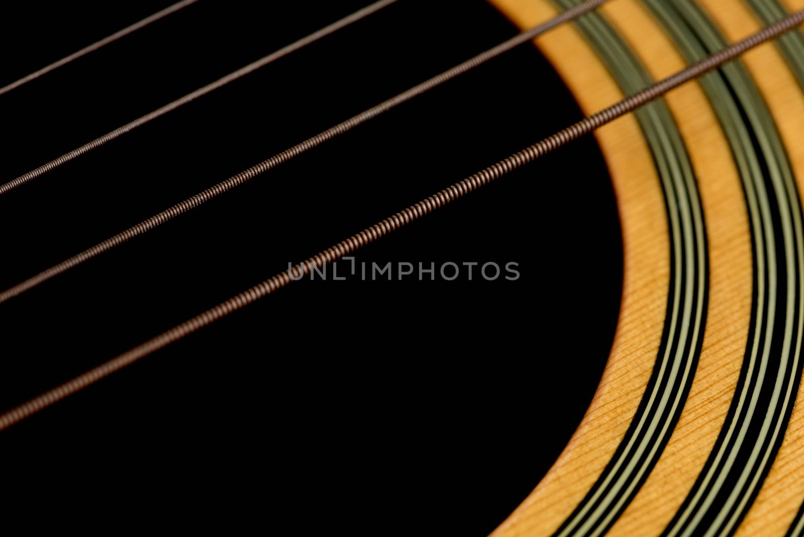An angled macro shot of acoustic guitar strings and the wood around the sound hole of the guitar.