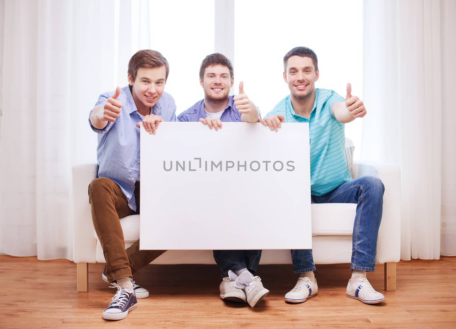 friendship, information and home concept - happy male friends with blank white board showing thumbs up at home