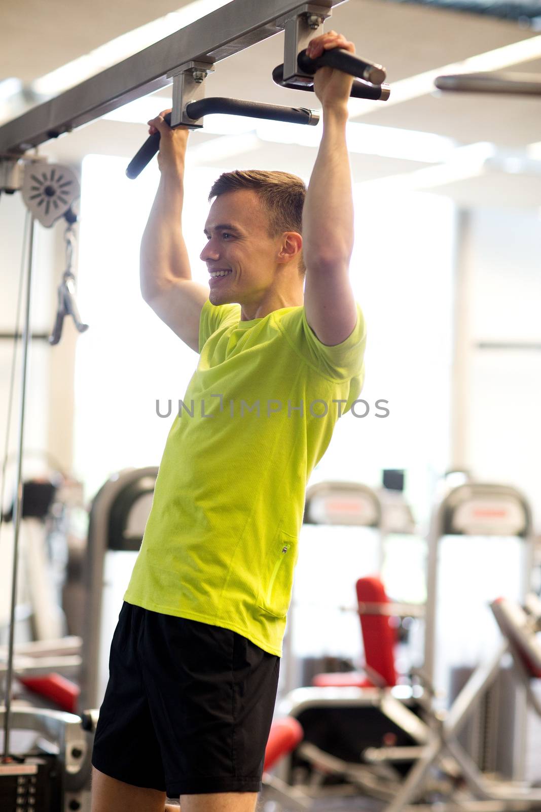 sport, fitness, lifestyle and people concept - smiling man doing pull-ups in gym