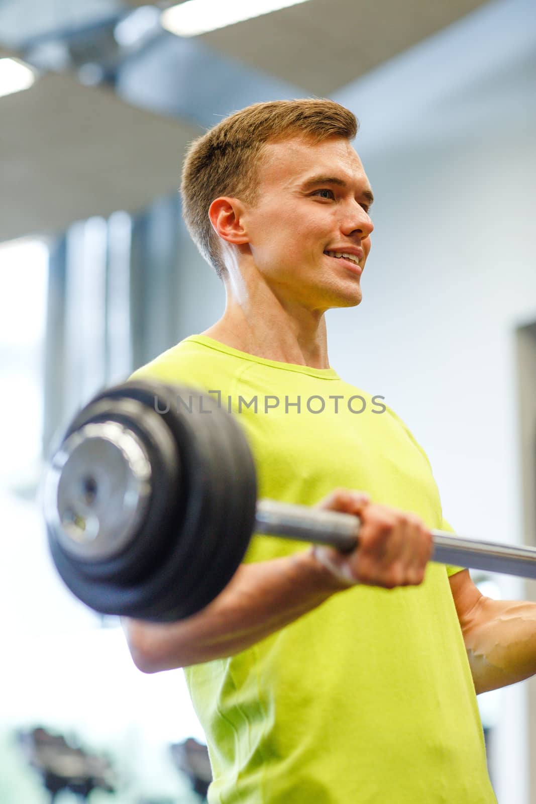 smiling man doing exercise with barbell in gym by dolgachov