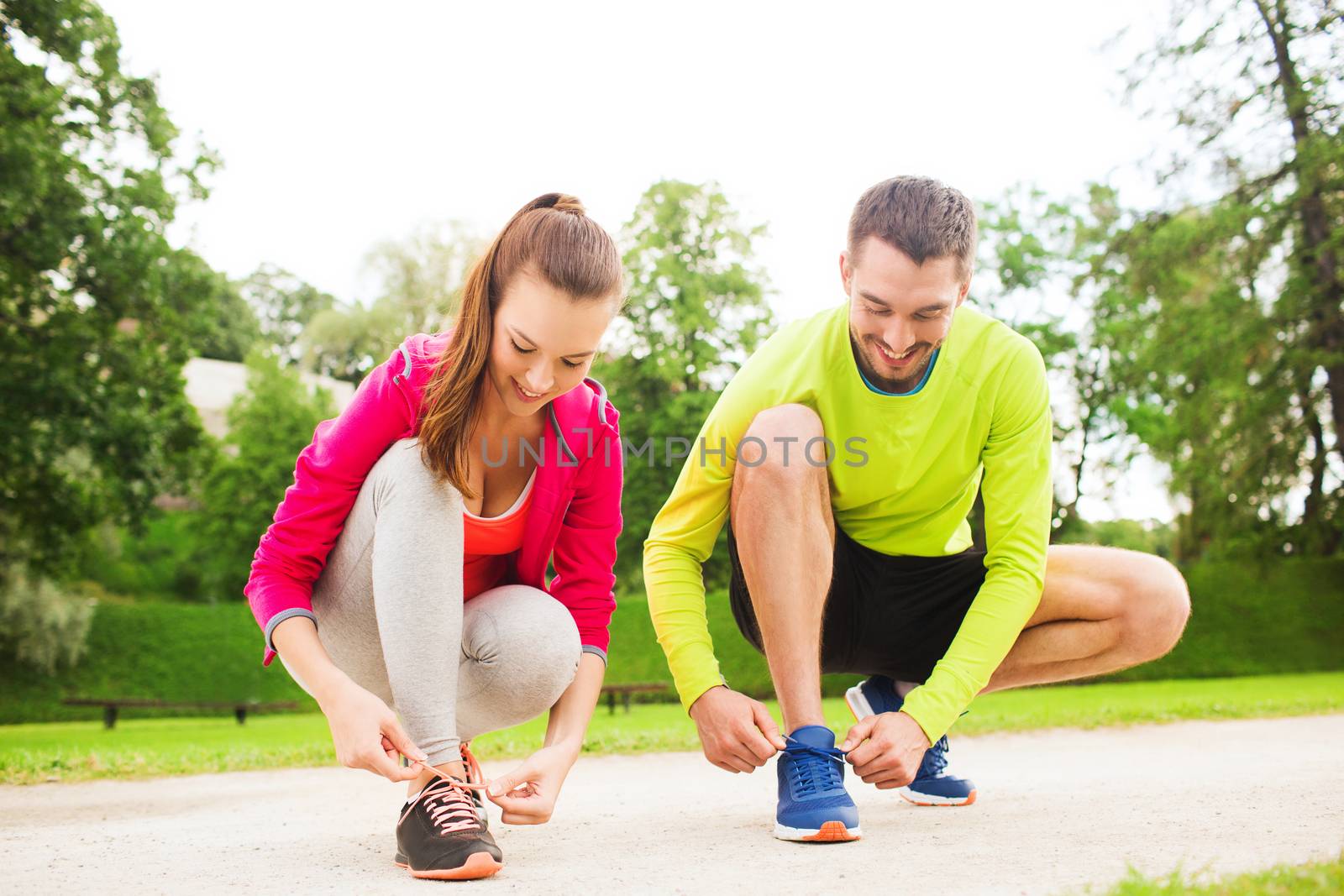 smiling couple tying shoelaces outdoors by dolgachov