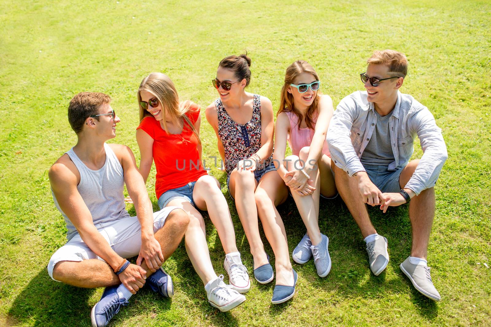 friendship, leisure, summer and people concept - group of smiling friends outdoors sitting and talking on grass on grass in park