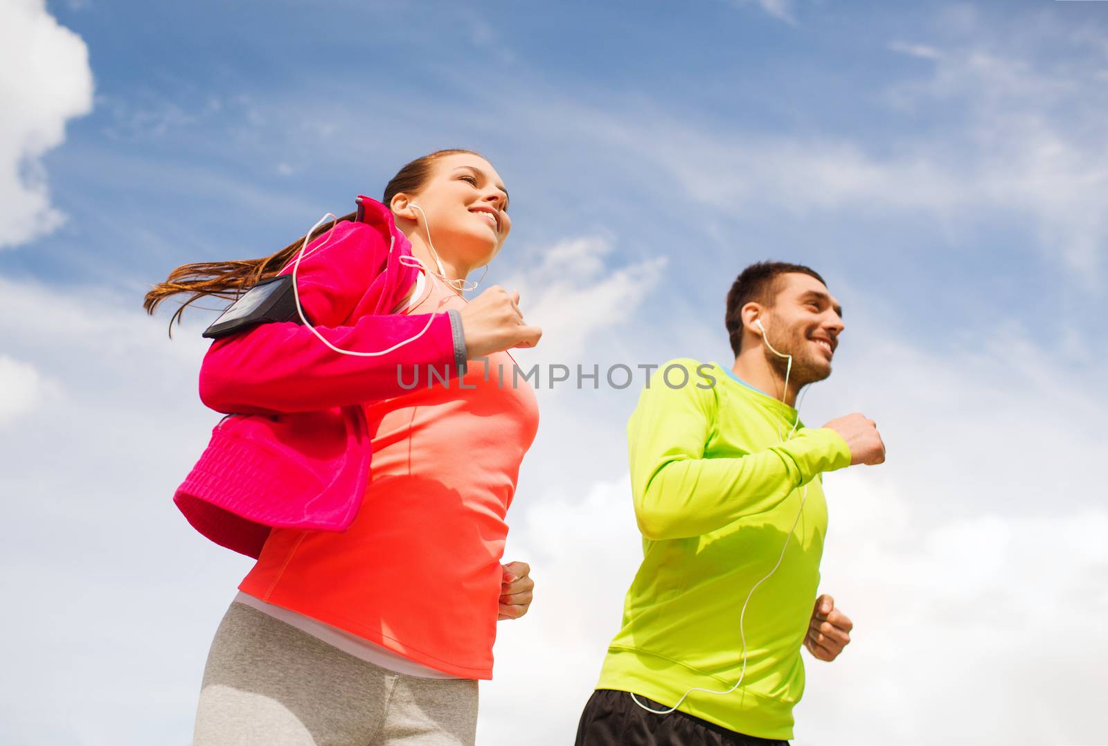 fitness, sport, friendship and lifestyle concept - smiling couple with earphones running outdoors