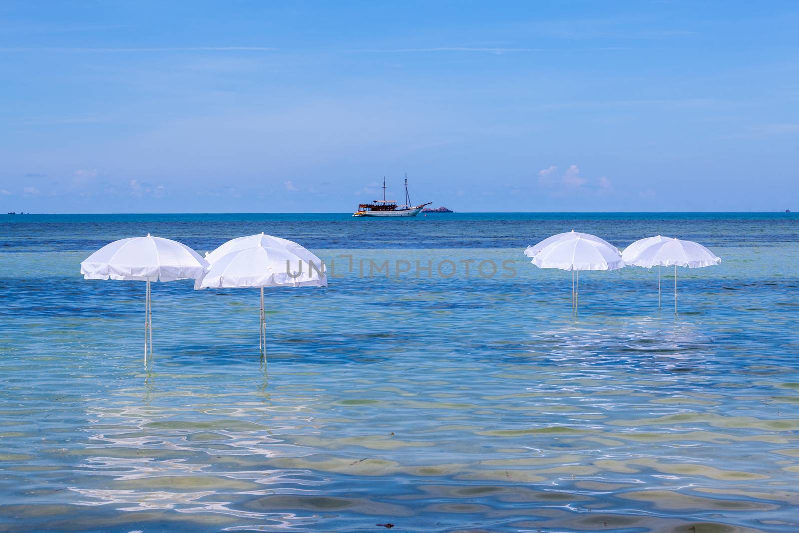 White umbrella on summer tropical beach with sailing boat.