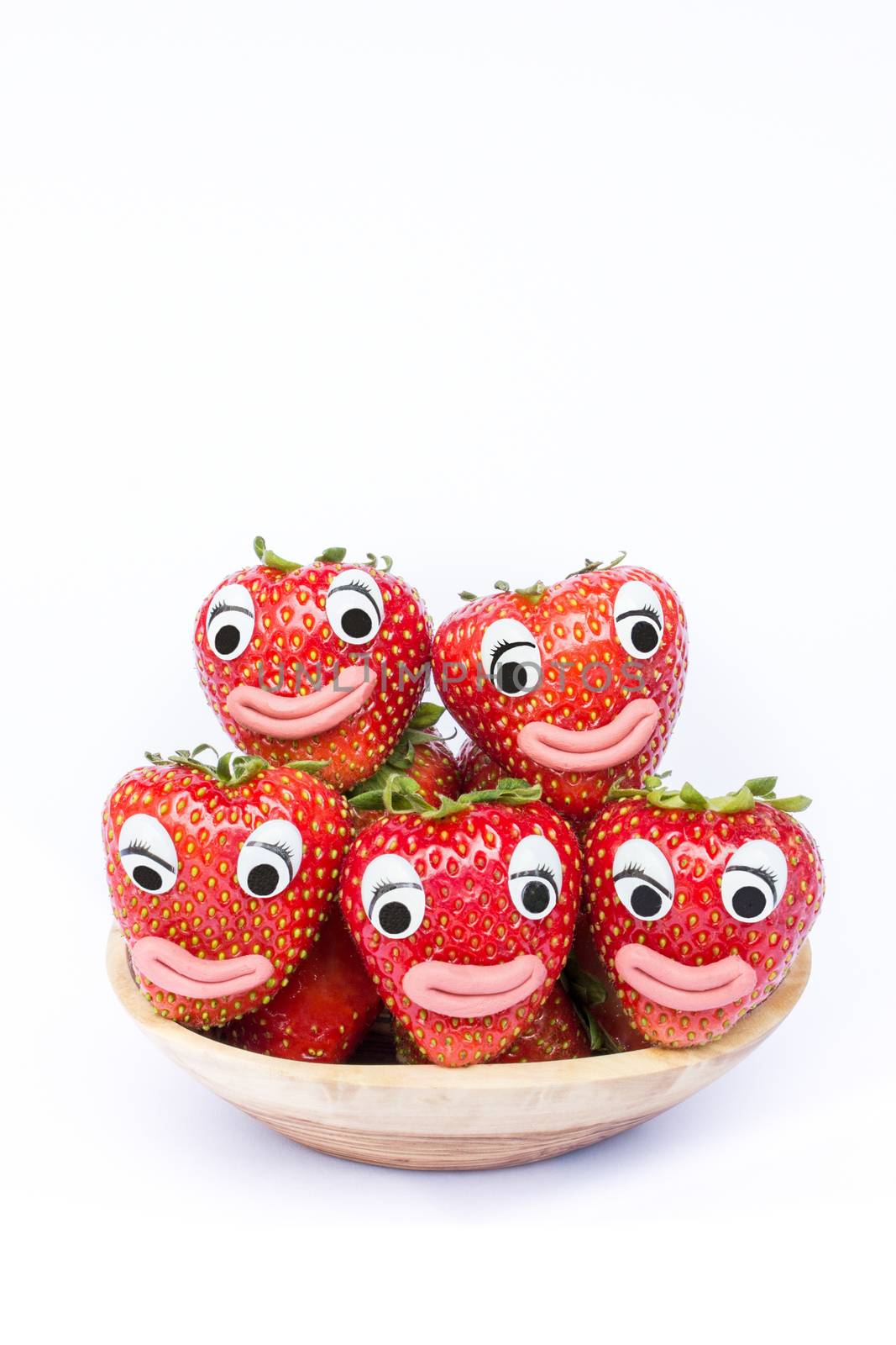 stack of red strawberries on wooden scale. Fruit with eyes and mouths isolated on white background