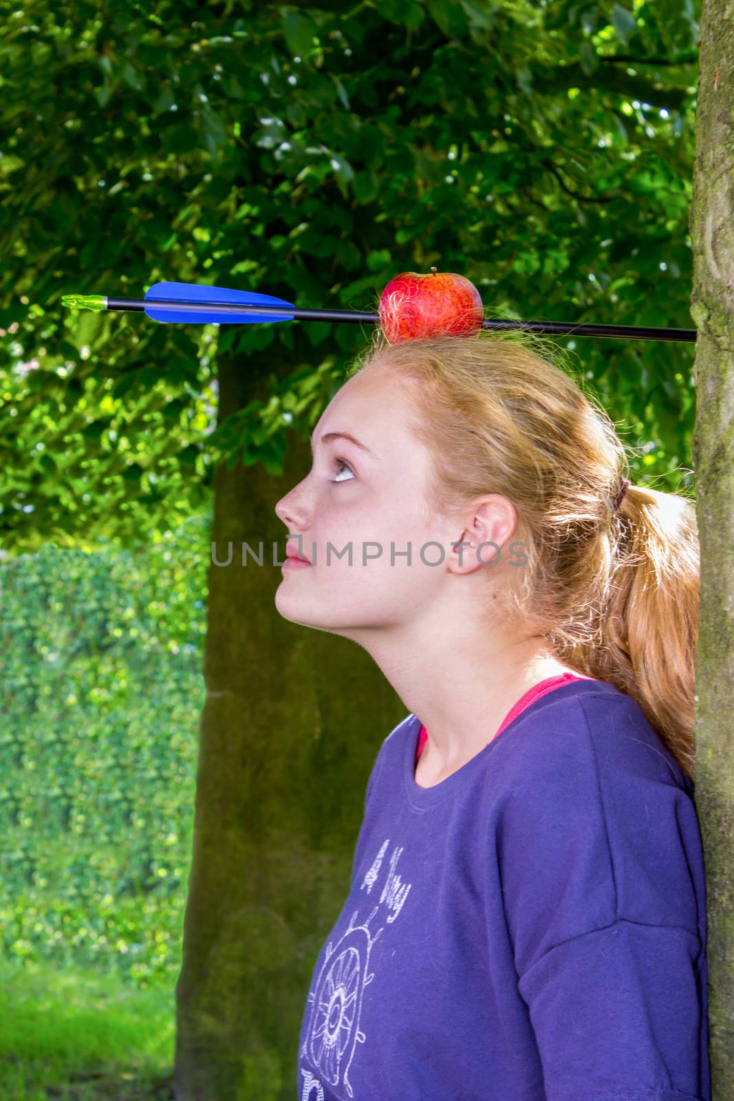 Girl with apple and arrow on her head standing outdoors