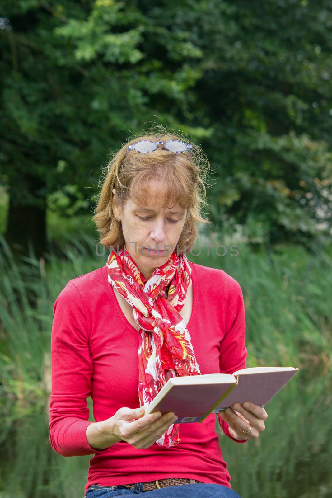 Woman reading book in front of green reed and trees