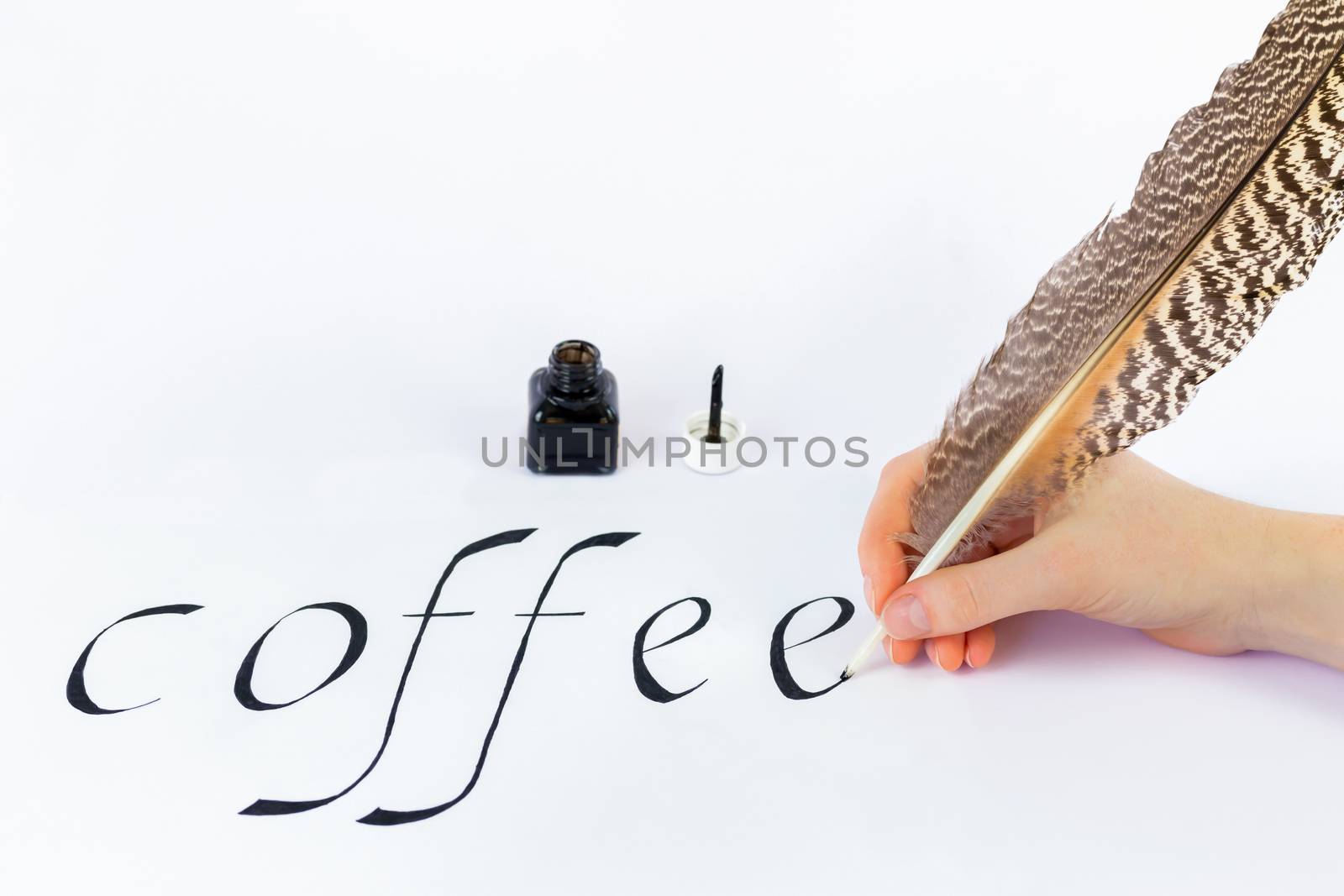 Hand holding bird feather writing the word coffee with black ink on white paper