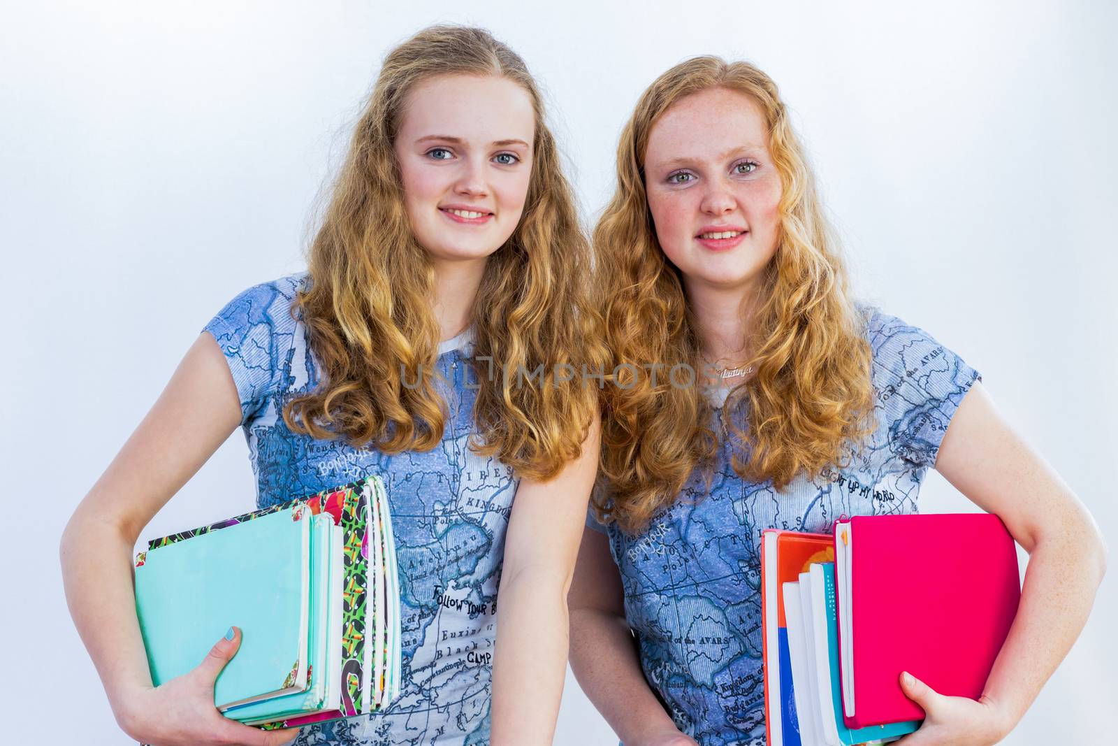 Two caucasian choolgirls carrying school books under the arms isolated on white background