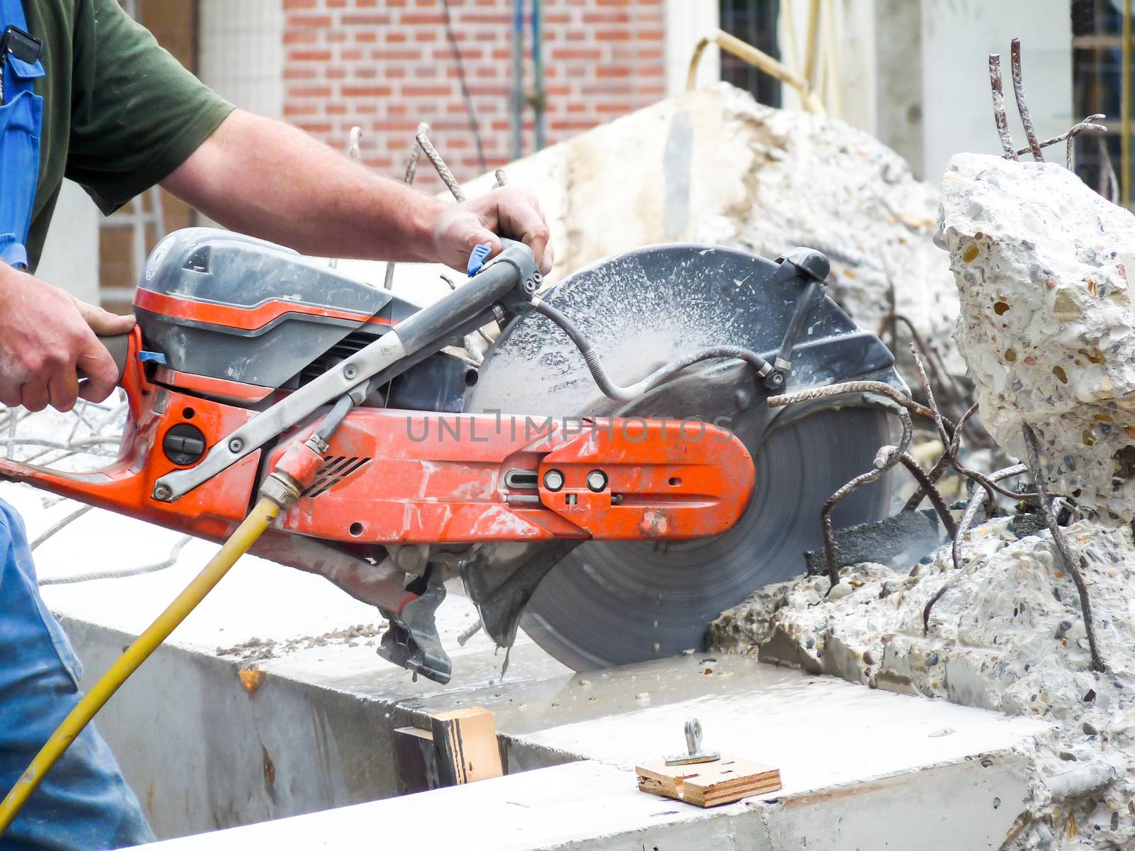 Arms of construction worker holding grinder cutting concrete