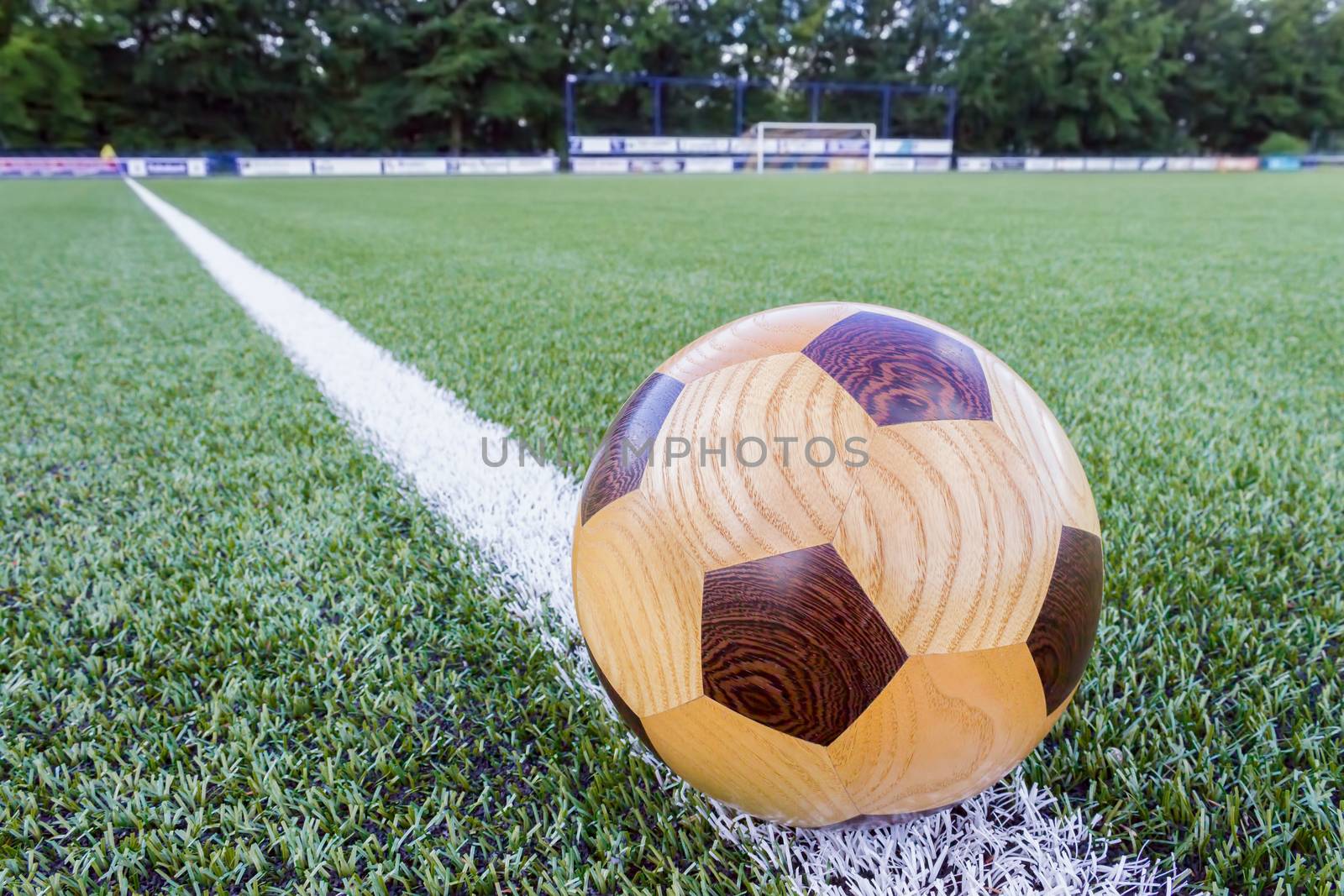Wooden football lying on sideline with goal in background
