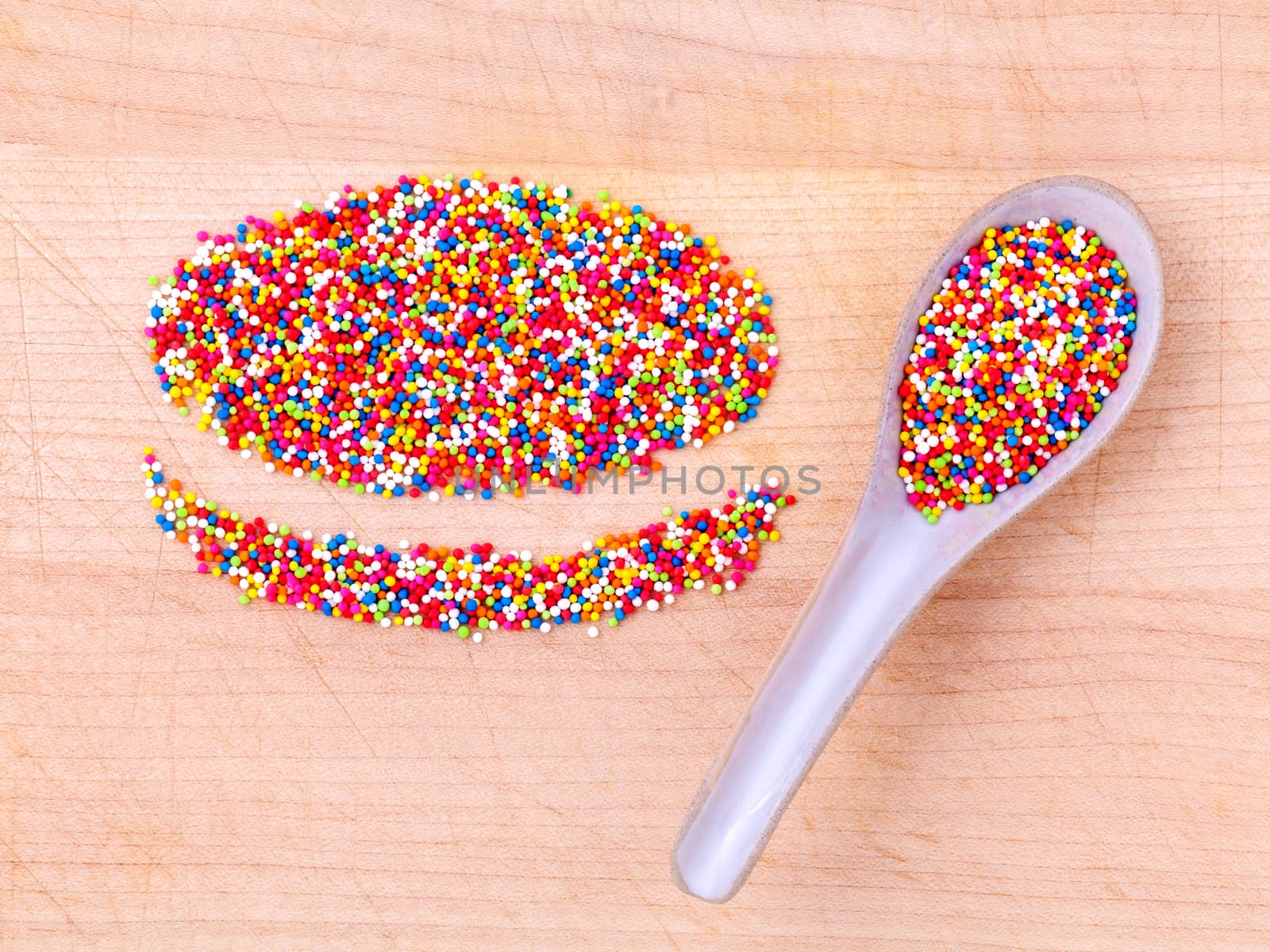 Colourful topping baking in wooden spoon and the shape of macaroons on wooden table.