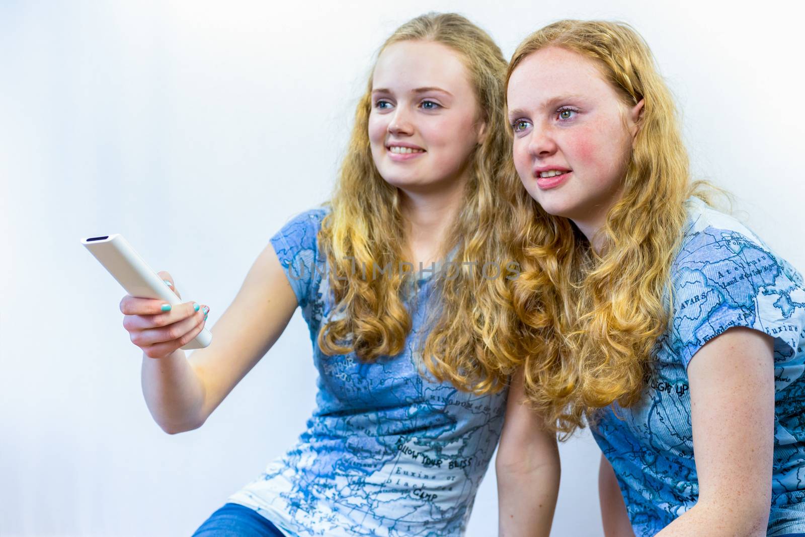 Two caucasian teenage sisters holding remote control watching TV isolated on white background