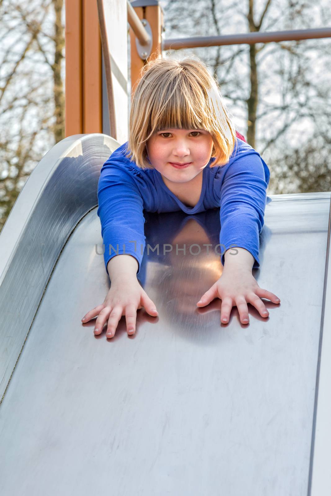 Young caucasian girl lies forward on slide at playground