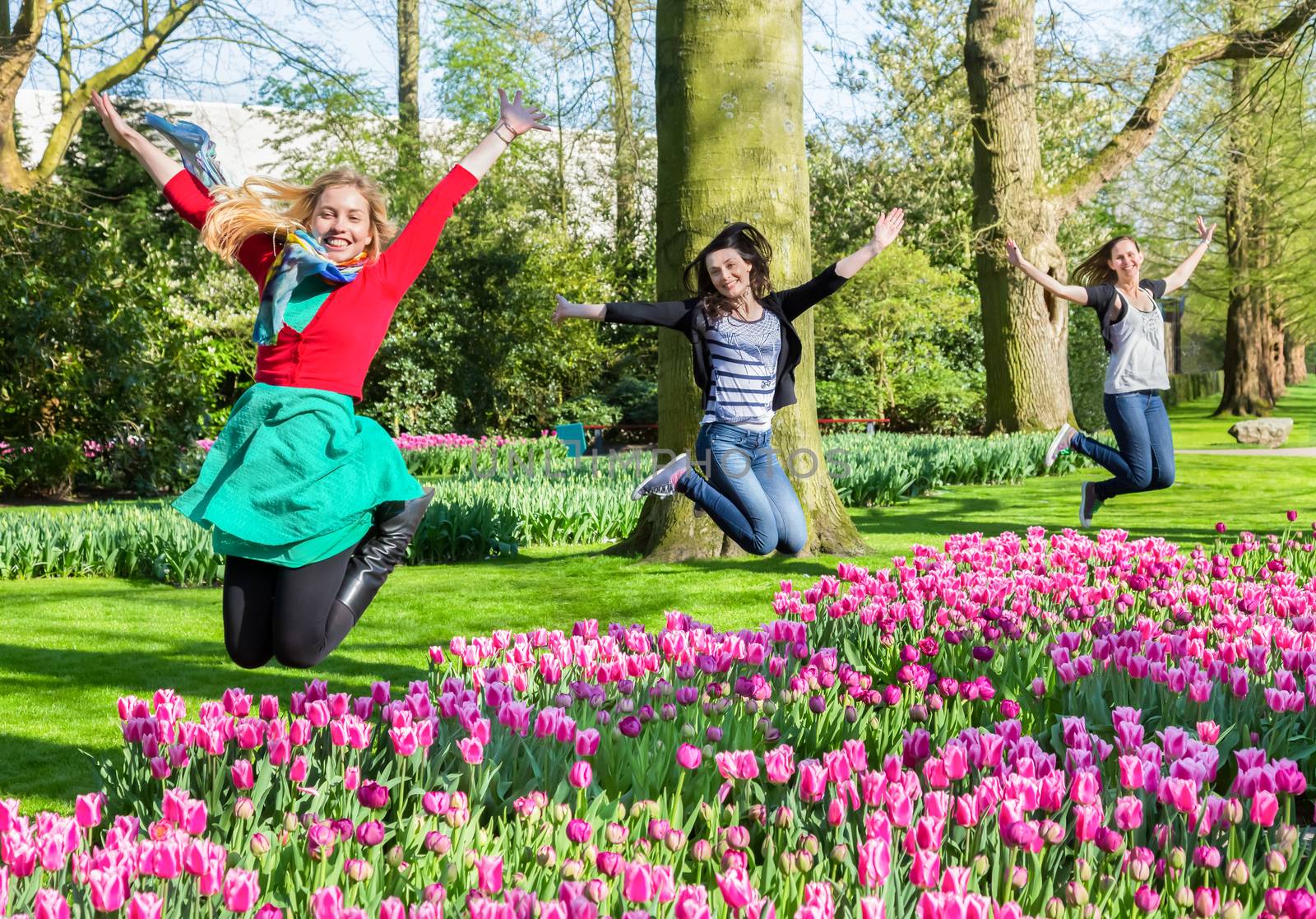 Three caucasian girls jumping above flowers field in Keukenhof Holland