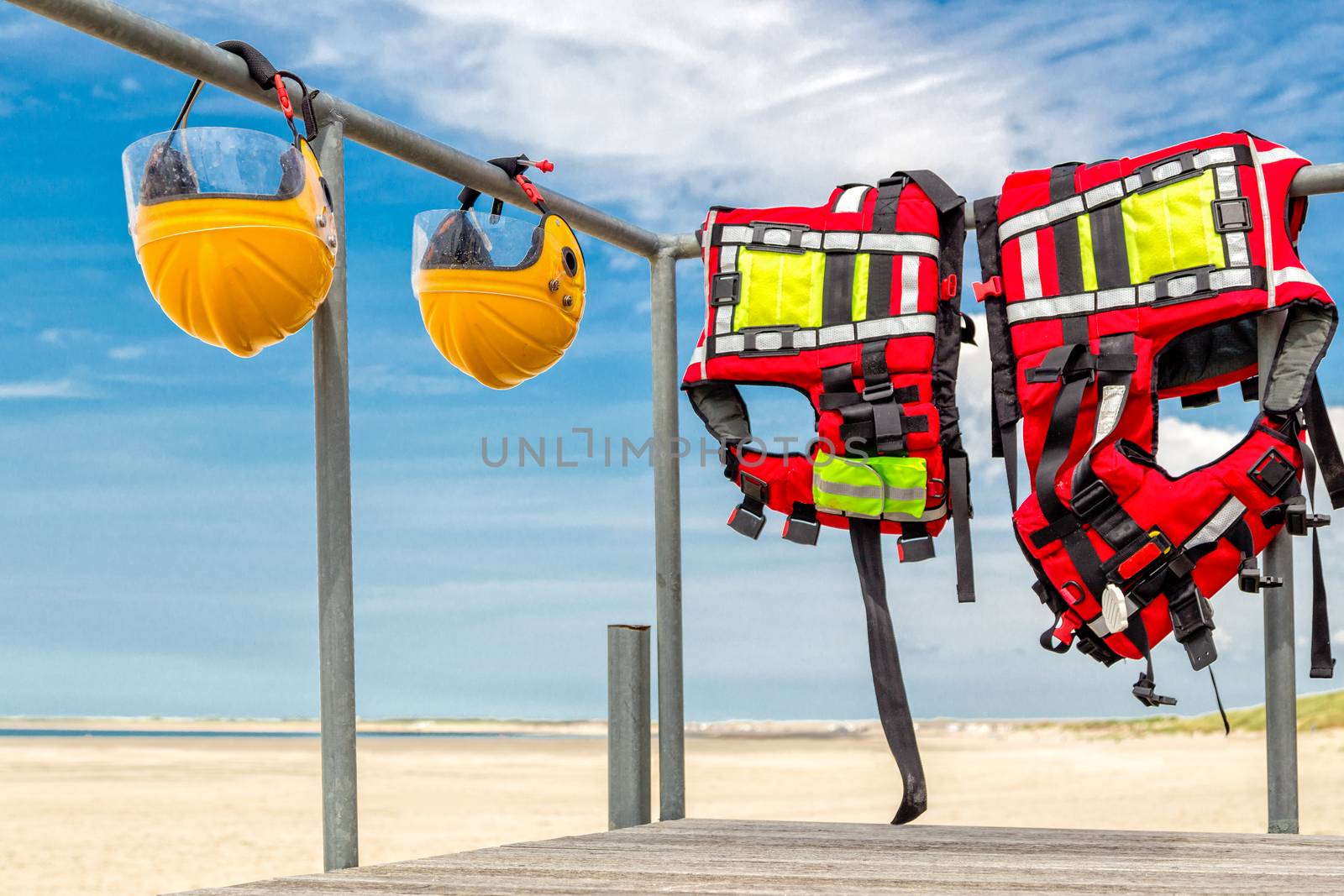 Safety helmets and life jackets hanging on railing near beach at coast