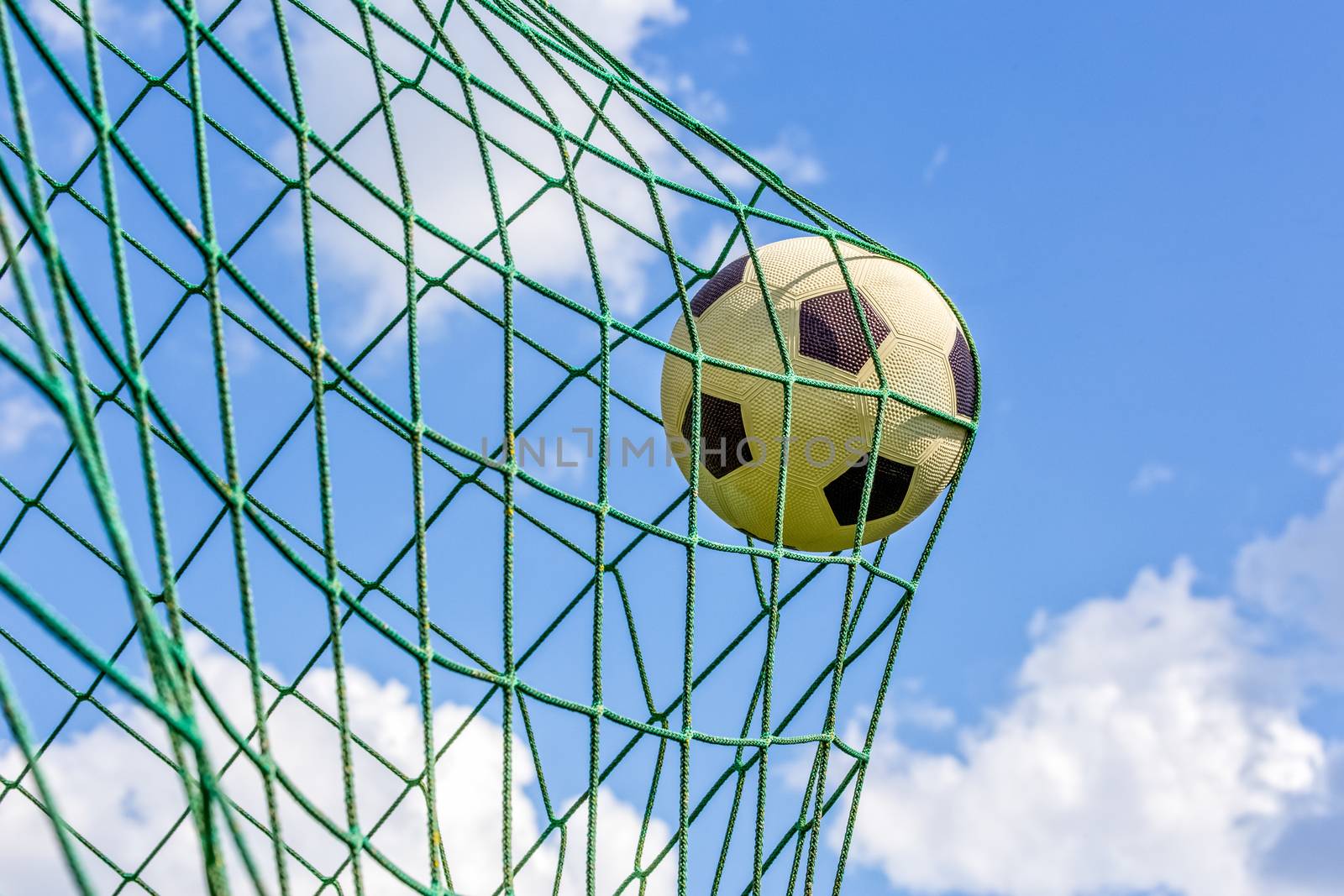 Black and white football shot in goal net in front of blue sky with white clouds