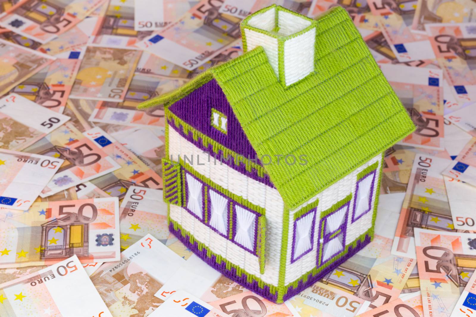 Embroidered little model house on table filled with euro money