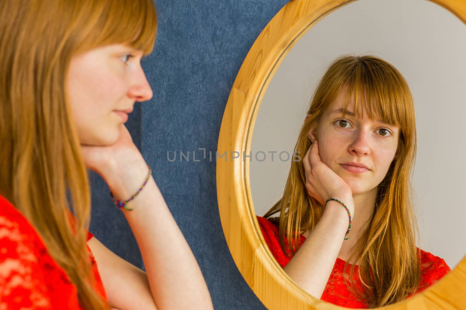 Redhead teenage girl looking in mirror by BenSchonewille