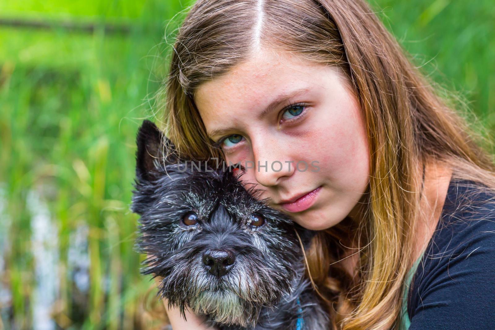 Blonde caucasian teenage girl hugging and loving black dog in nature