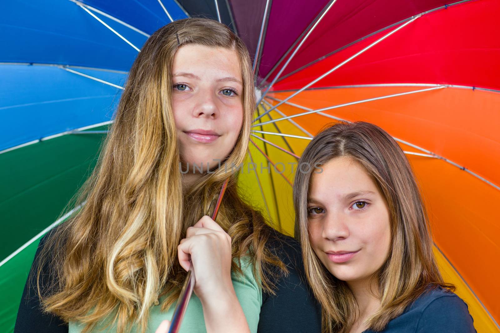 Two caucasian  teenage sisters together under colorful umbrella