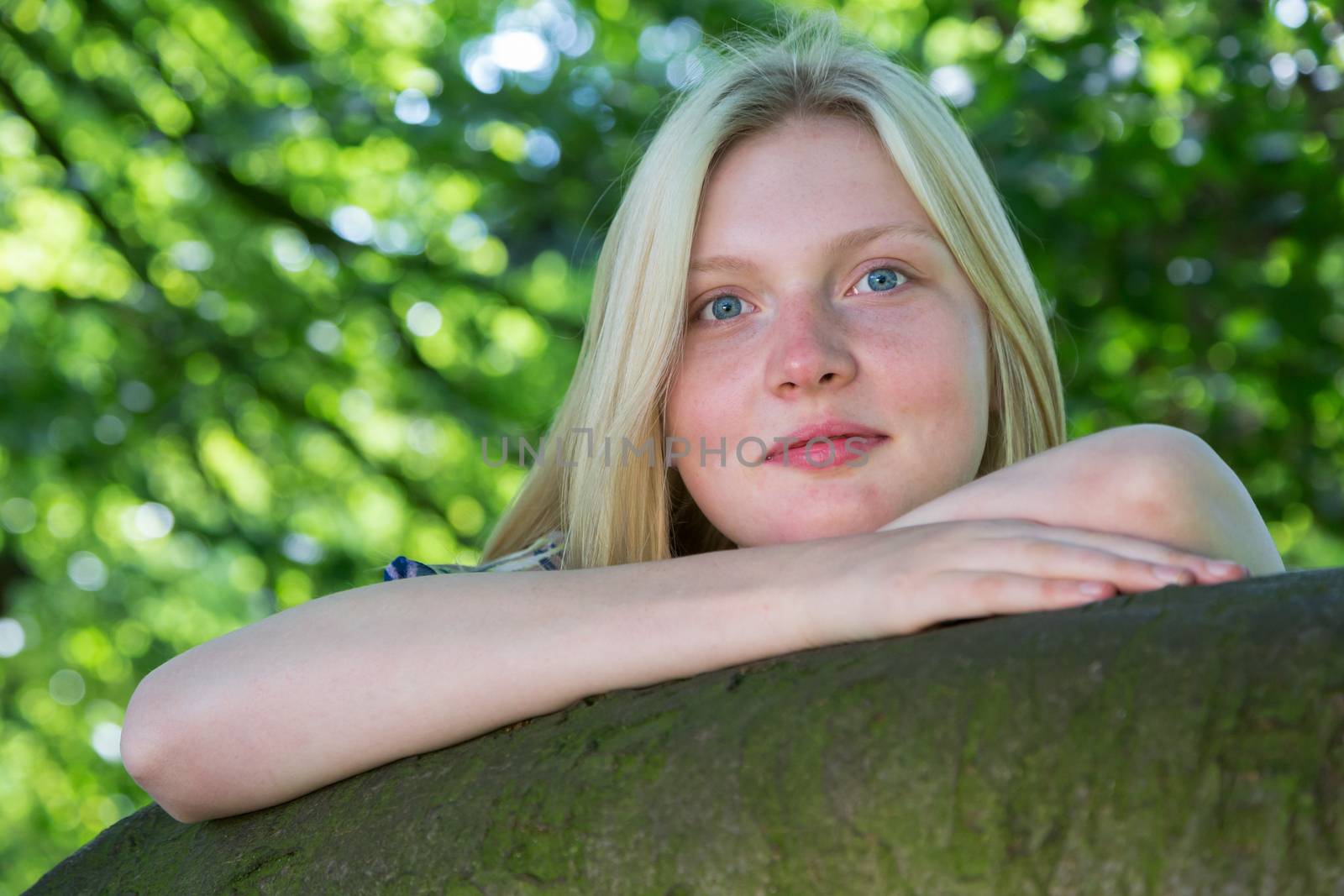 Blonde caucasian teenage girl leaning on branch of tree in nature