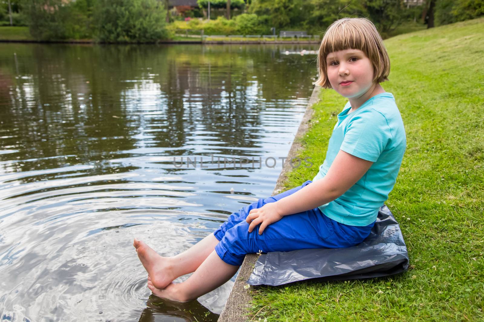 Young dutch girl sitting with feet in water of  pond in park