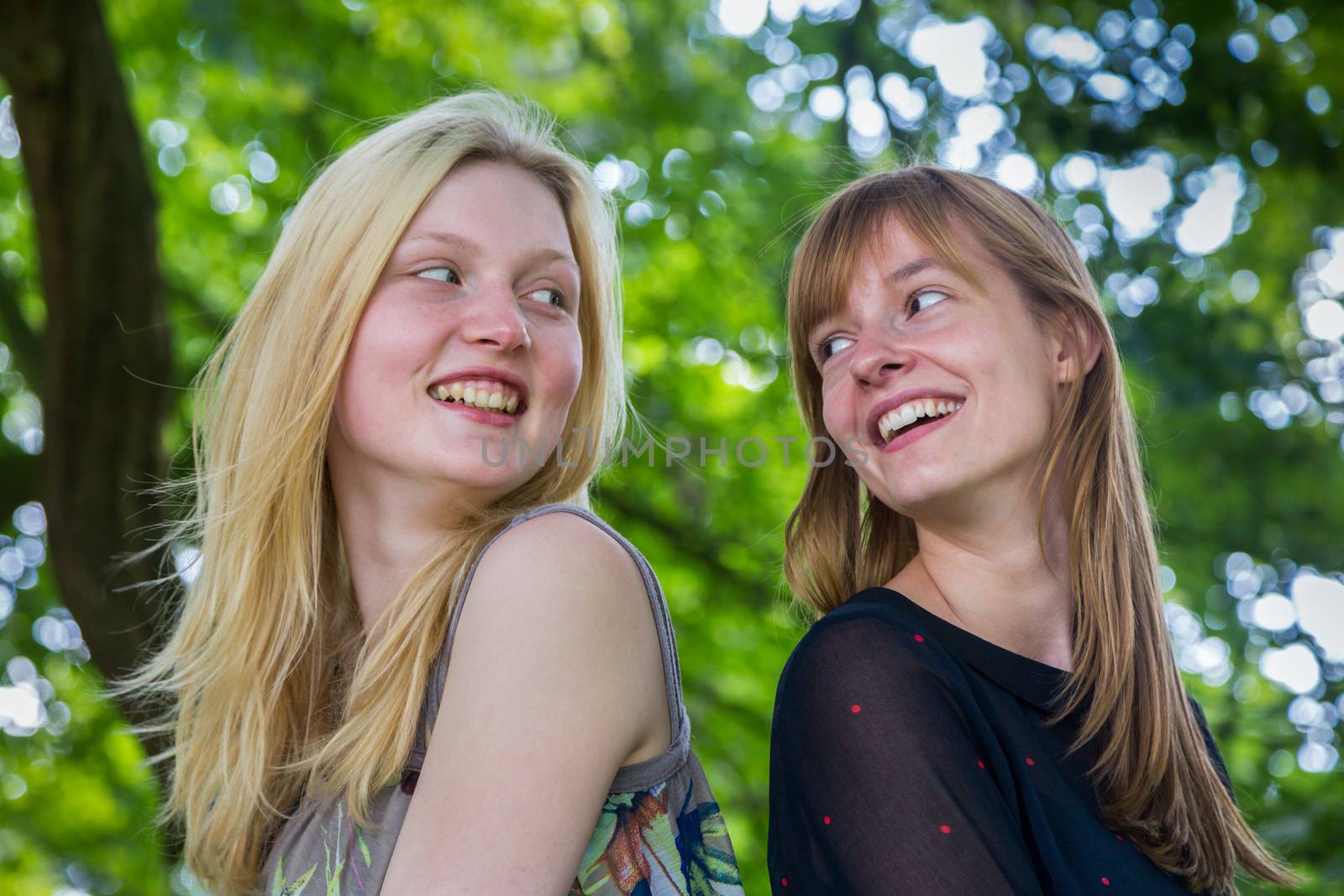 Two long-haired dutch teenage girls laughing to each other with tree background