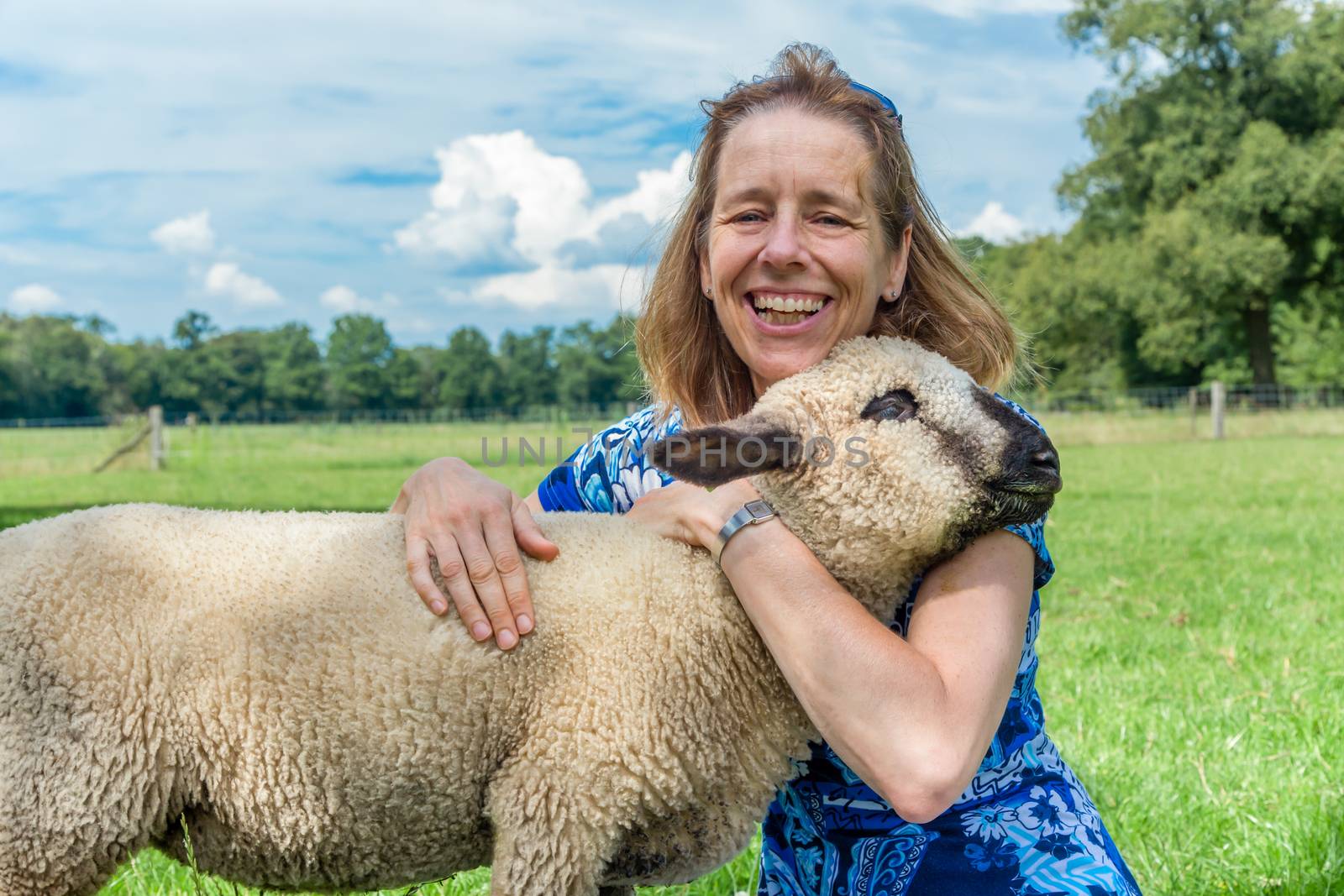 European woman embracing and hugging sheep in meadow