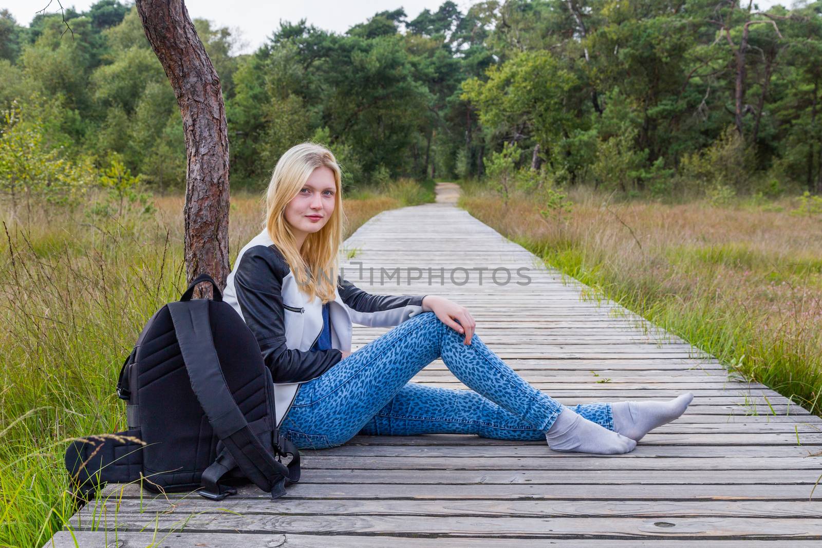 Blonde girl resting on wooden path in nature by BenSchonewille