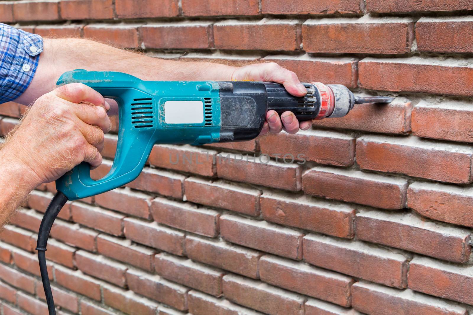 Arms holding drilling machine against brick wall by BenSchonewille