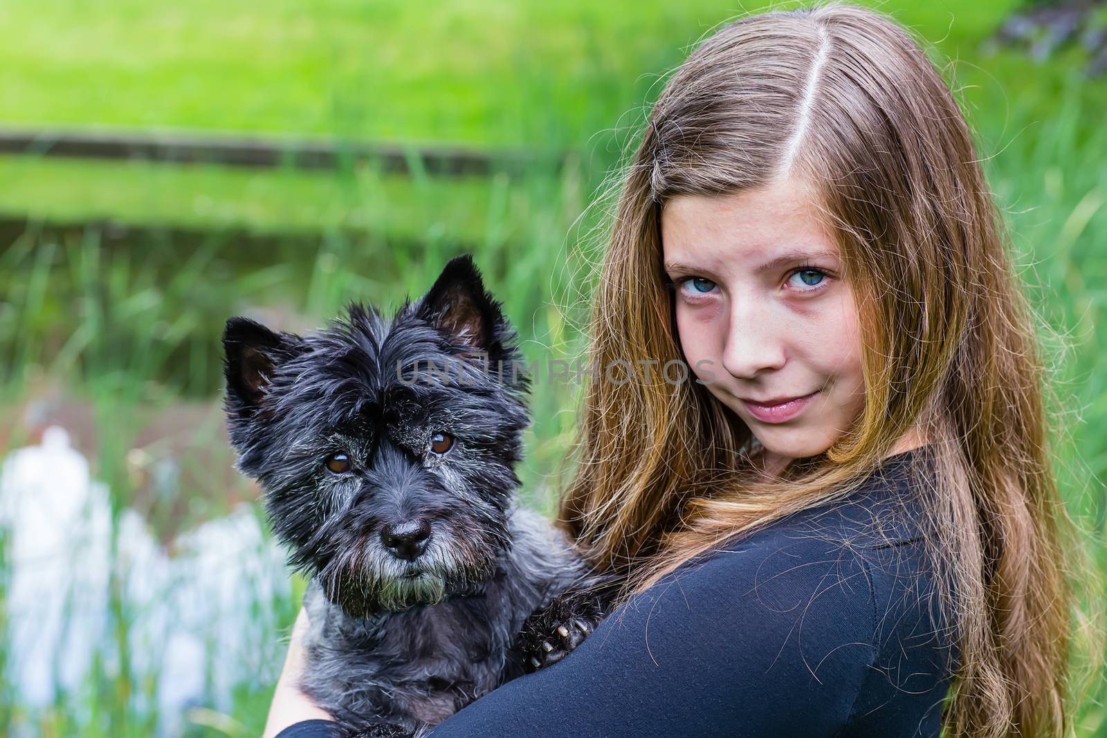 Girl carrying black dog on arm in park by BenSchonewille