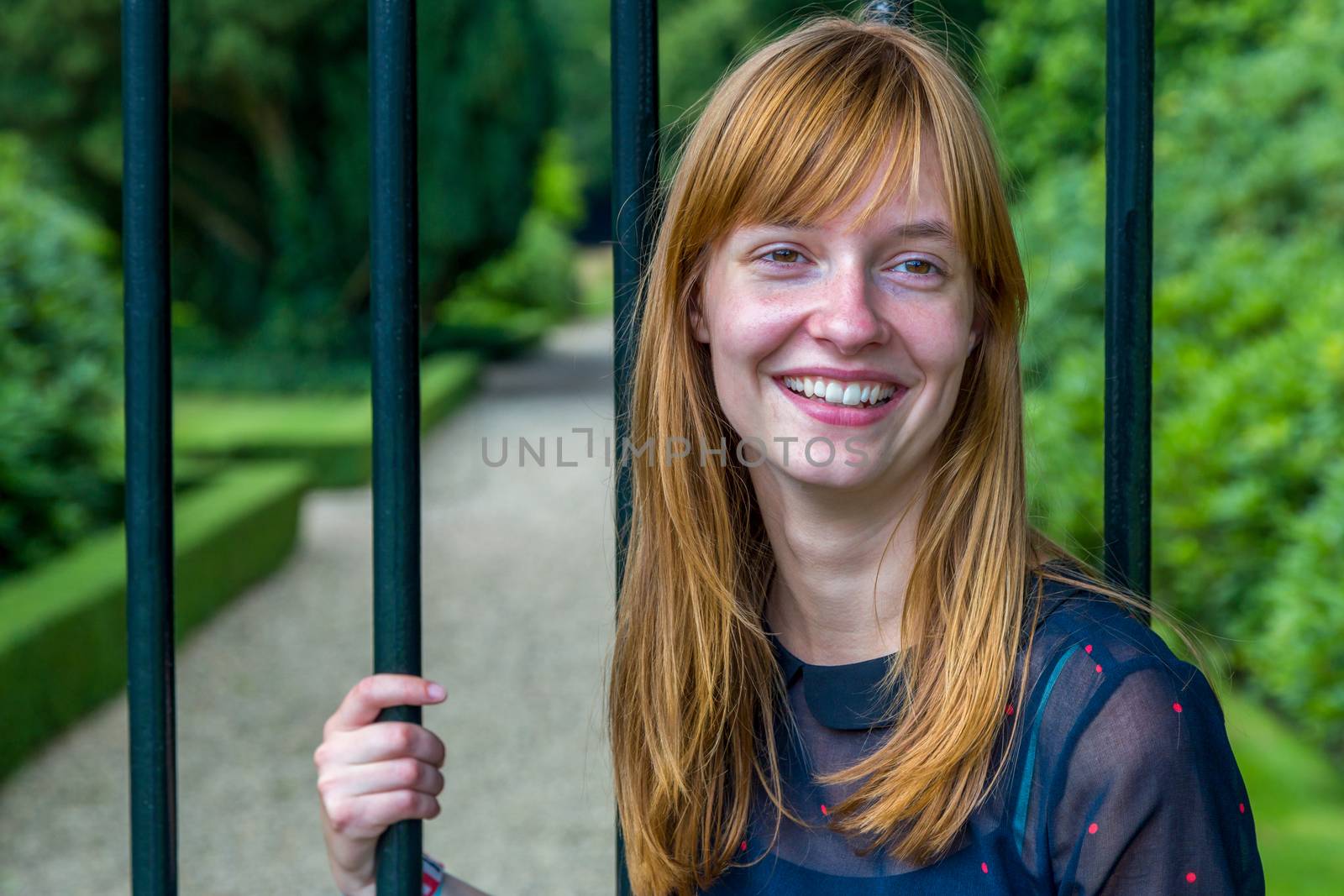 Redhead girl laughing holding bar gate by BenSchonewille